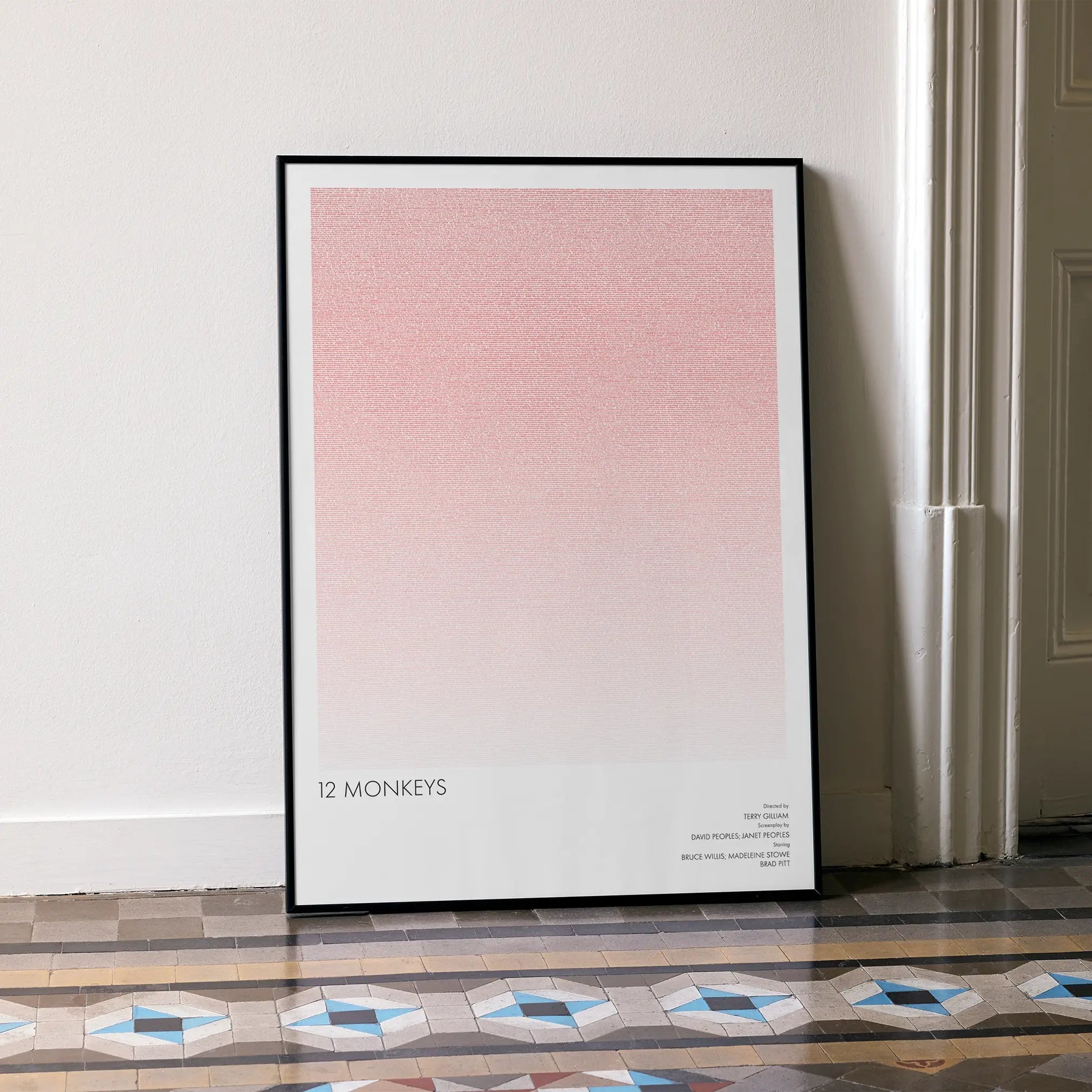 A framed 12 Monkeys movie script poster leaning against a wall in a minimalist interior.