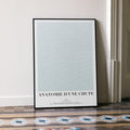 A framed Anatomie d'une chute movie script poster leaning against a wall in a minimalist interior.