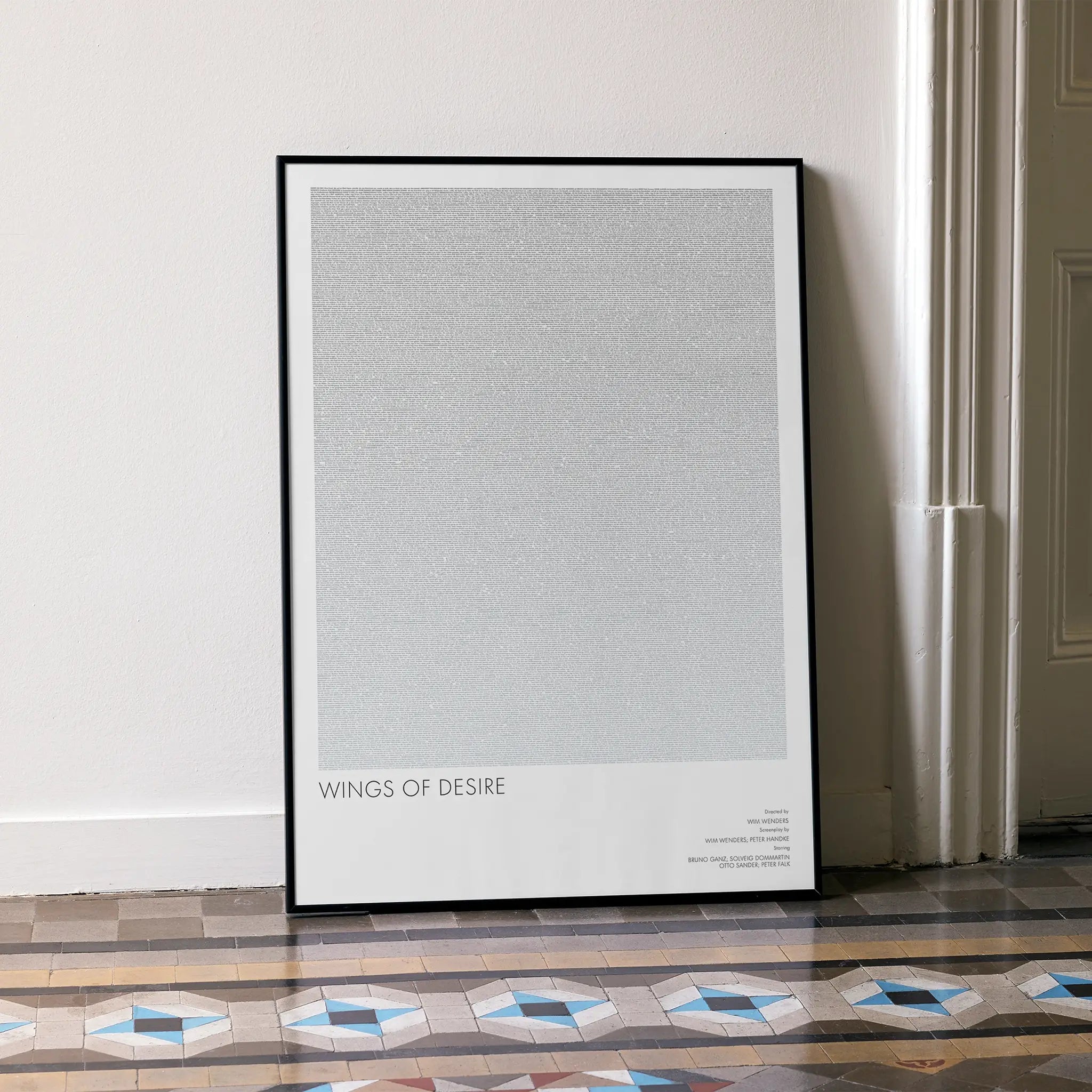 A framed Wings of Desire movie script poster leaning against a wall in a minimalist interior.
