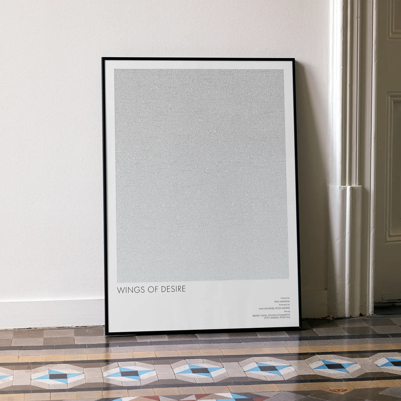 A framed Wings of Desire movie script poster leaning against a wall in a minimalist interior.