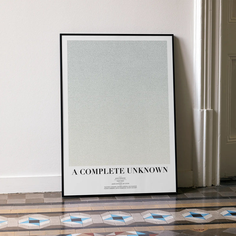 A framed A Complete Unknown movie script poster leaning against a wall in a minimalist interior.