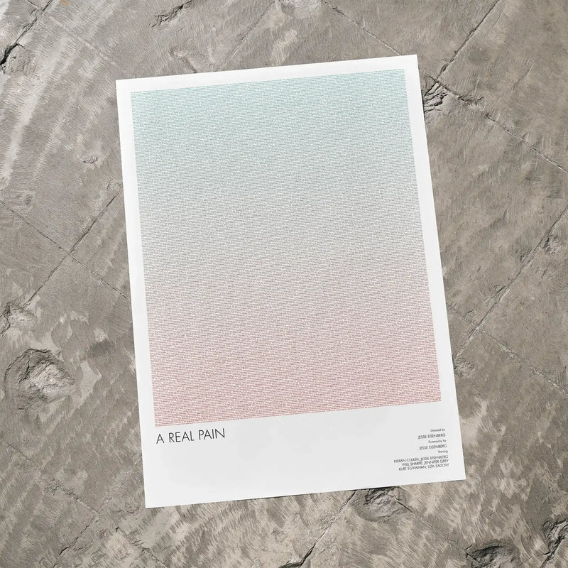 A A Real Pain movie script poster laid flat on a textured floor surface.