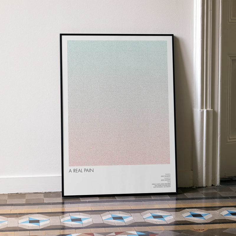 A framed A Real Pain movie script poster leaning against a wall in a minimalist interior.