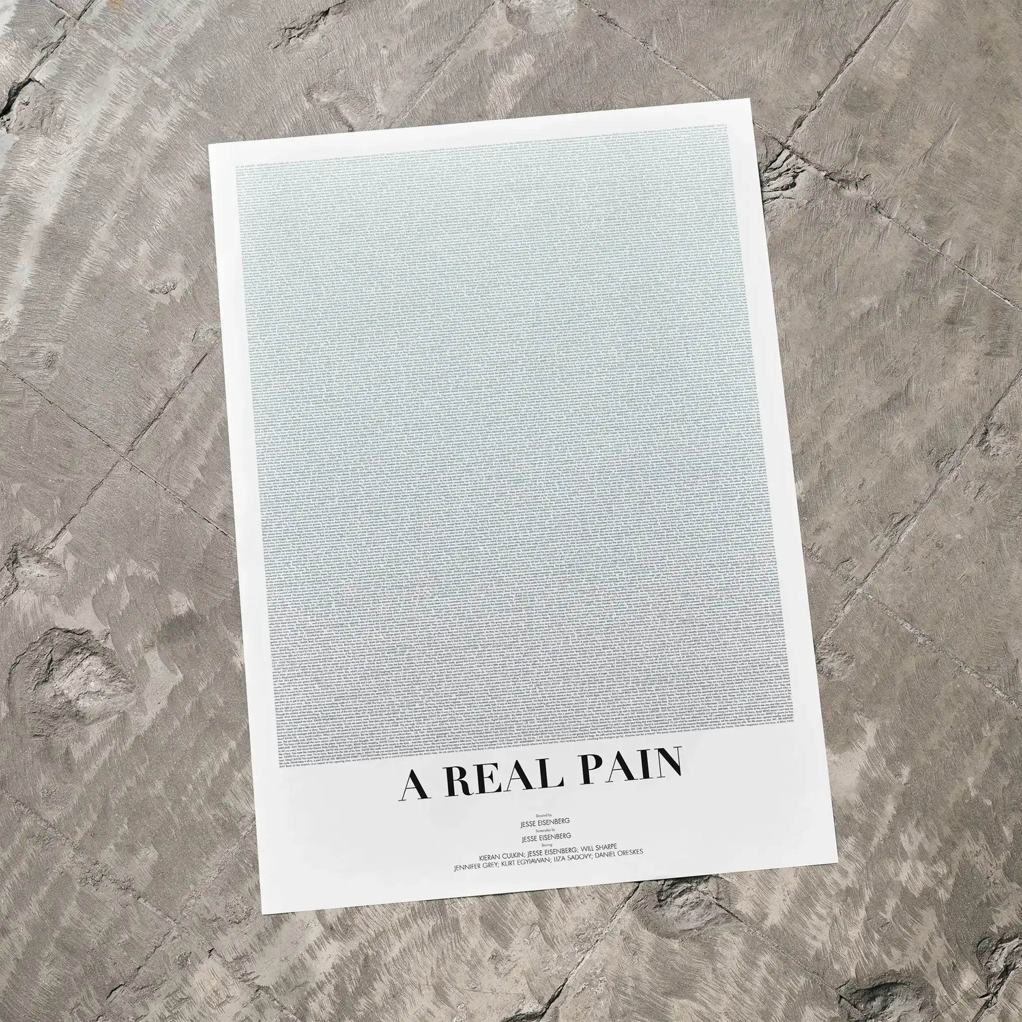 A A Real Pain movie script poster laid flat on a textured floor surface.