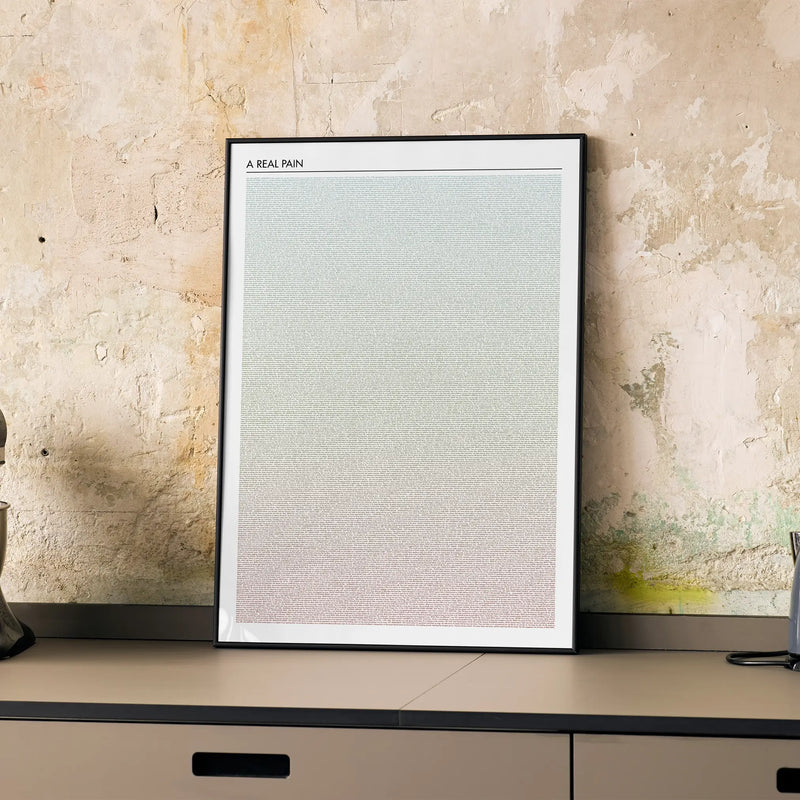 A framed A Real Pain movie script poster displayed on a cabinet in a minimalist interior.
