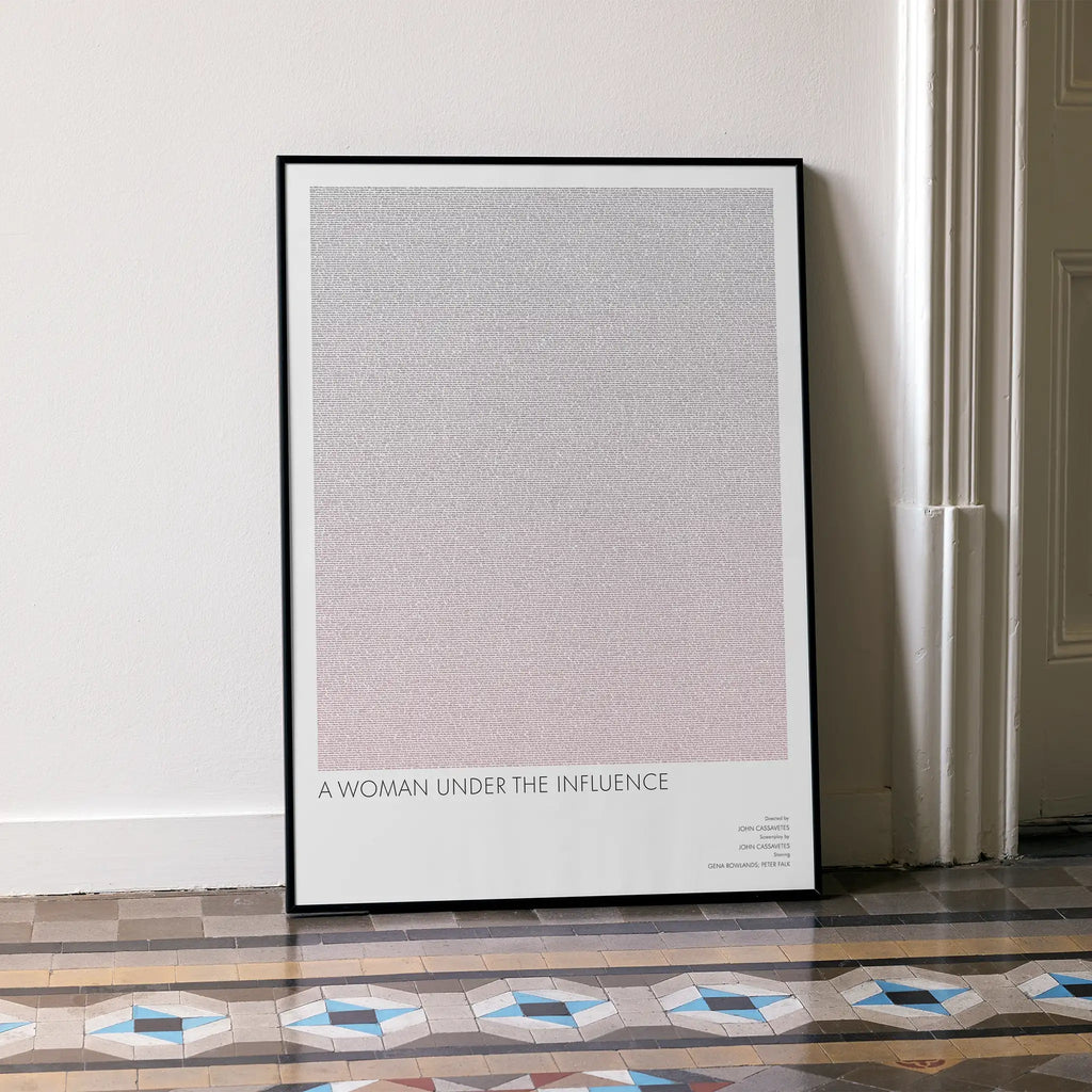 A framed minimalist art print leaning against a white wall on a patterned tiled floor. The print features a large textured square in a soft gray-to-pale pink gradient with the text 'A WOMAN UNDER THE INFLUENCE' at the bottom.
