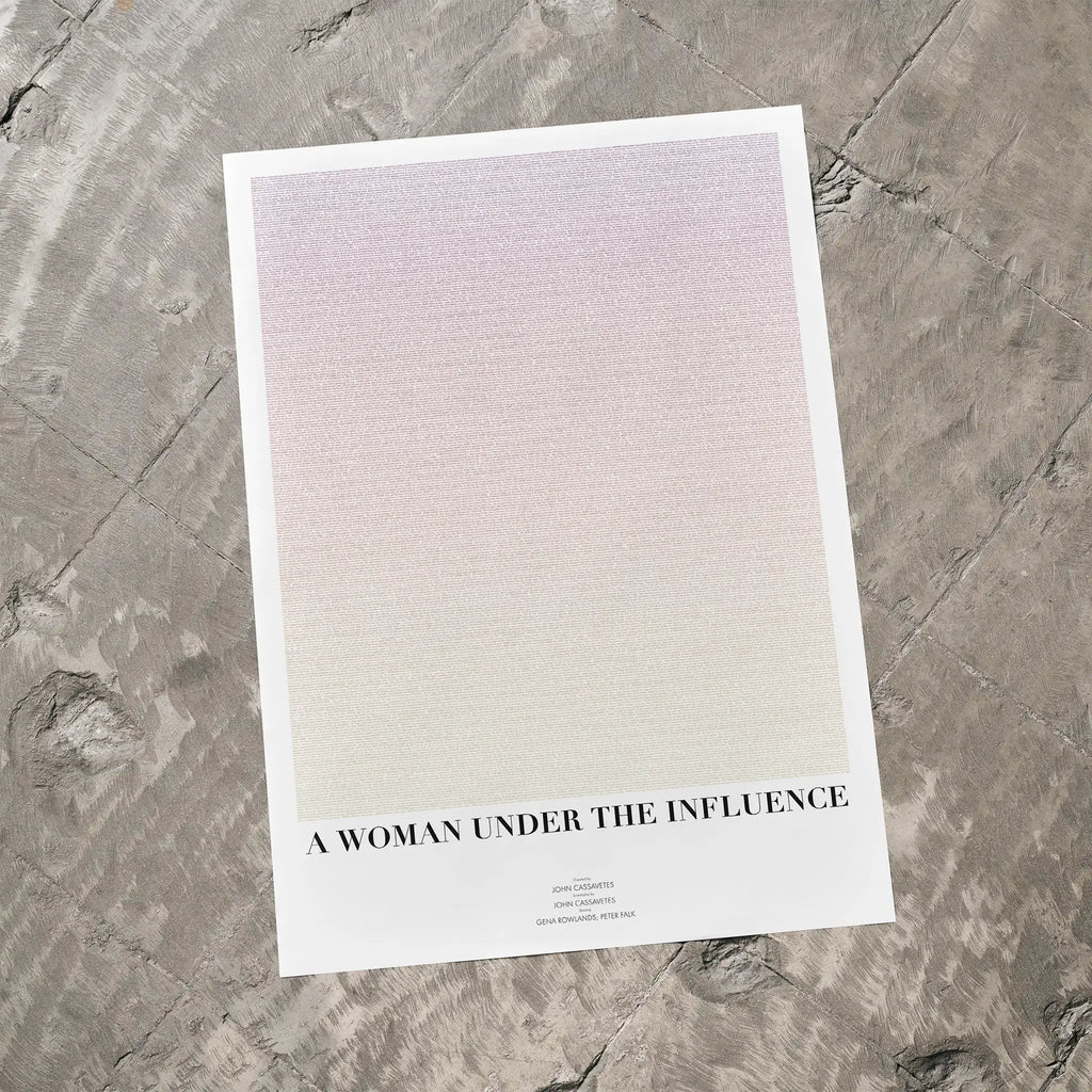 A minimalist art print titled 'A WOMAN UNDER THE INFLUENCE' by Fade Out Prints, featuring a soft pink-to-white gradient with black text, displayed on a textured gray stone surface.