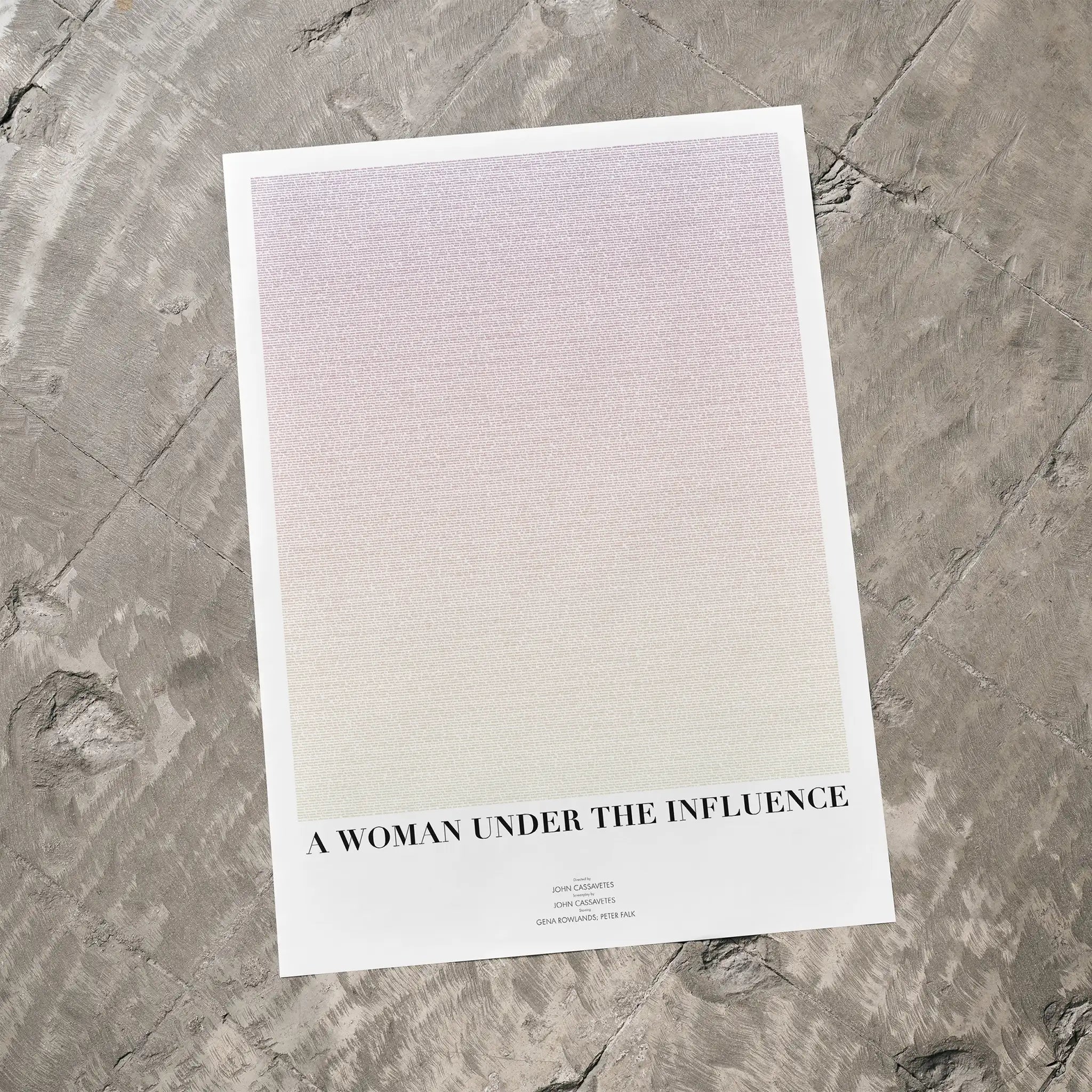 A minimalist art print titled 'A WOMAN UNDER THE INFLUENCE' by Fade Out Prints, featuring a soft pink-to-white gradient with black text, displayed on a textured gray stone surface.