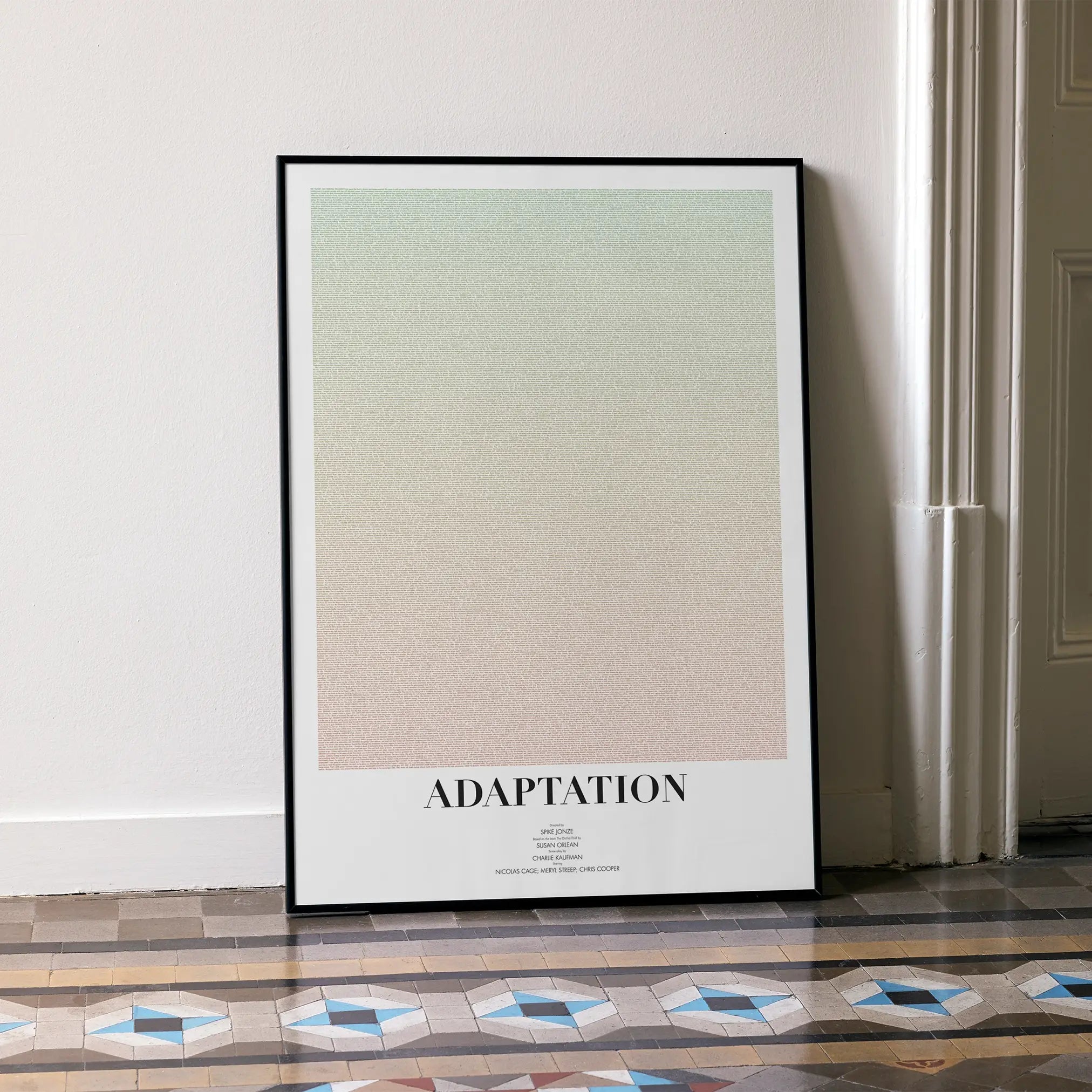 A framed Adaptation. movie script poster leaning against a wall in a minimalist interior.