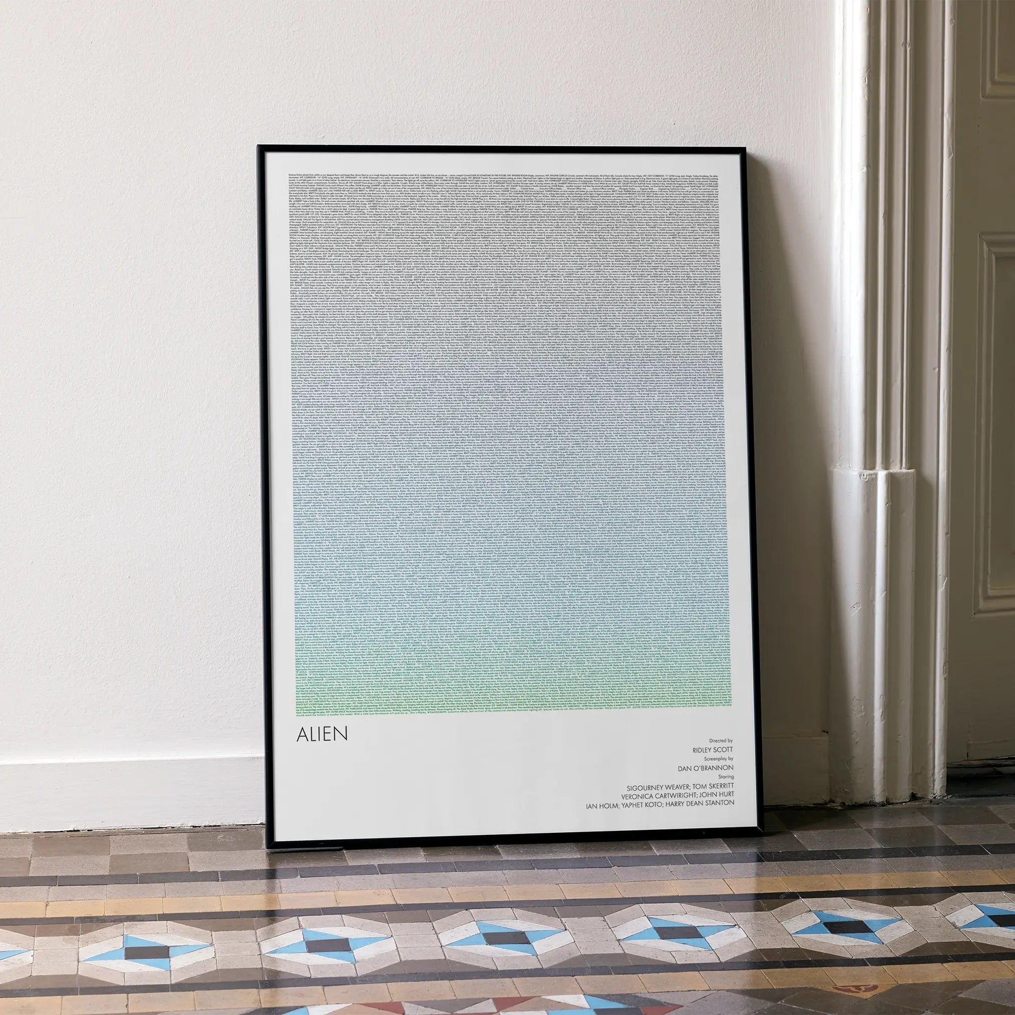 A framed Alien movie script poster leaning against a wall in a minimalist interior.