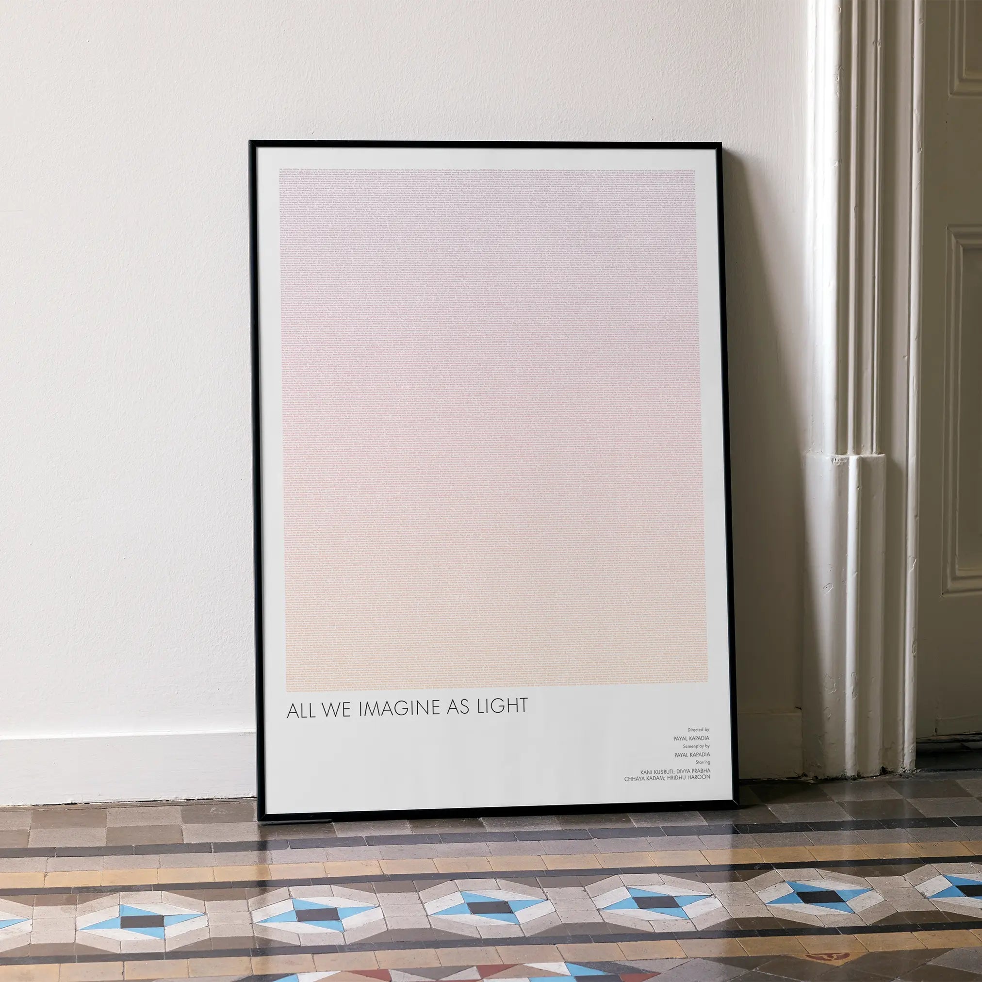 A framed All We Imagine as Light movie script poster leaning against a wall in a minimalist interior.