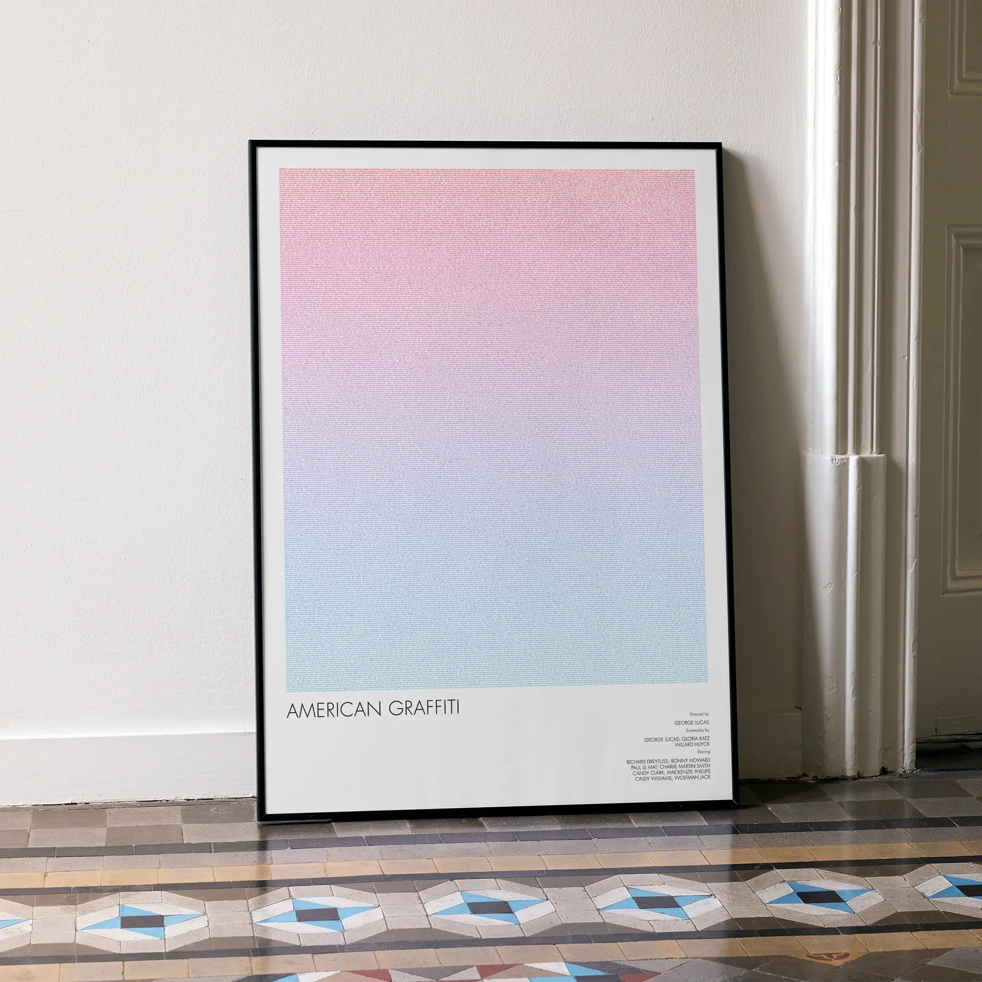 A framed American Graffiti movie script poster leaning against a wall in a minimalist interior.