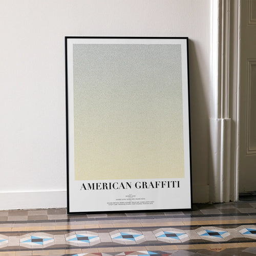 A framed American Graffiti movie script poster leaning against a wall in a minimalist interior.