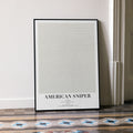 A framed American Sniper movie script poster leaning against a wall in a minimalist interior.