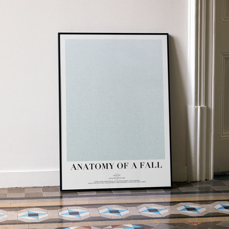 A framed Anatomy of a Fall movie script poster leaning against a wall in a minimalist interior.