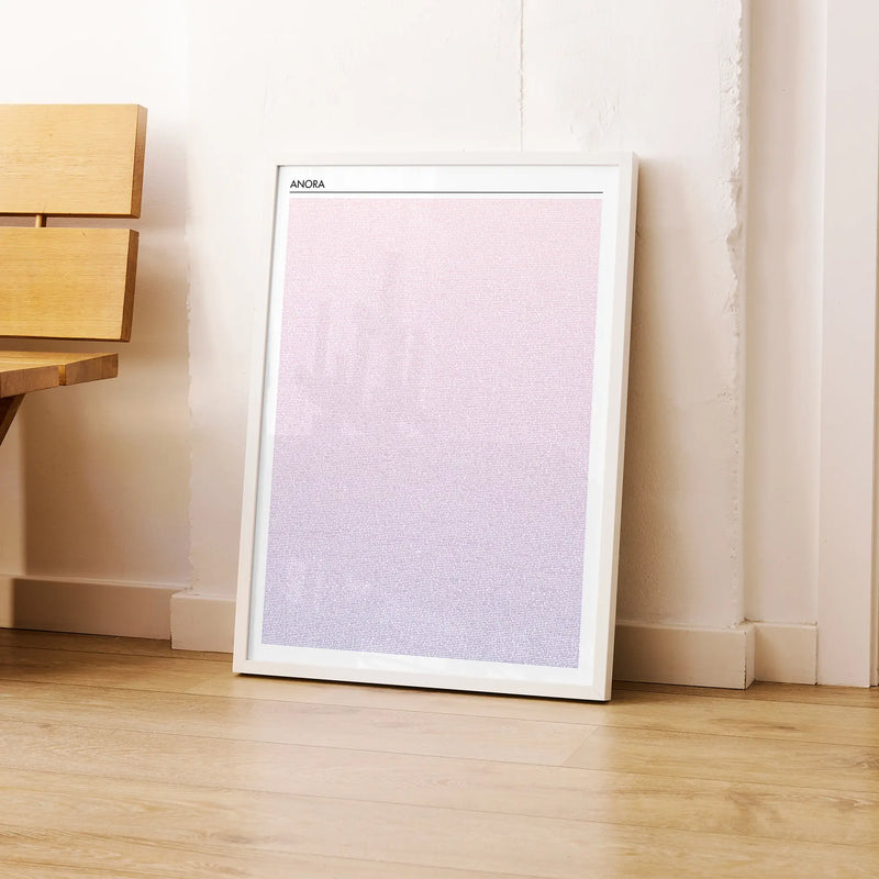 A framed Anora movie script poster leaning against a wall in a modern interior.