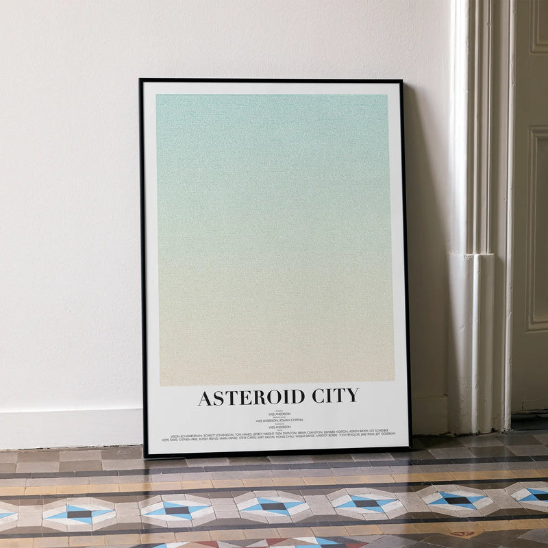 A framed Asteroid City movie script poster leaning against a wall in a minimalist interior.