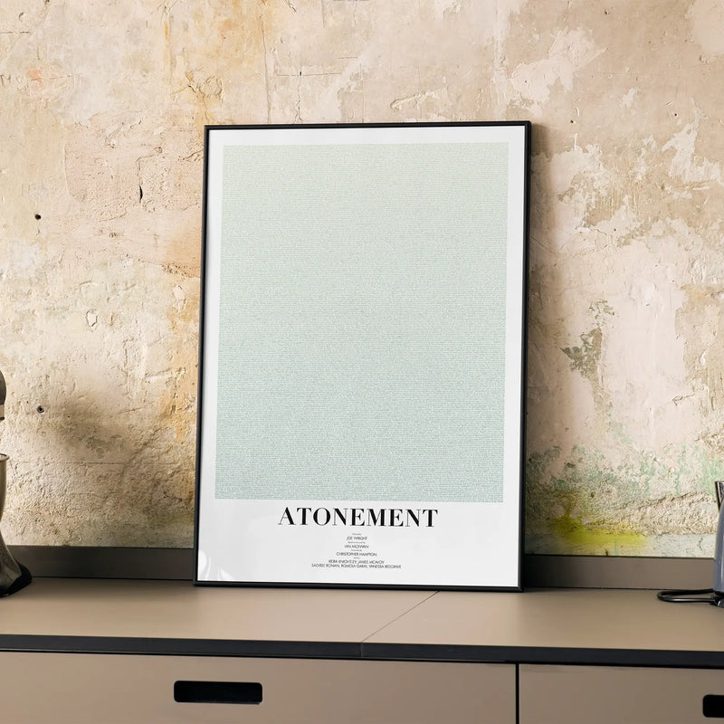 A framed Atonement movie script poster displayed on a cabinet in a minimalist interior.
