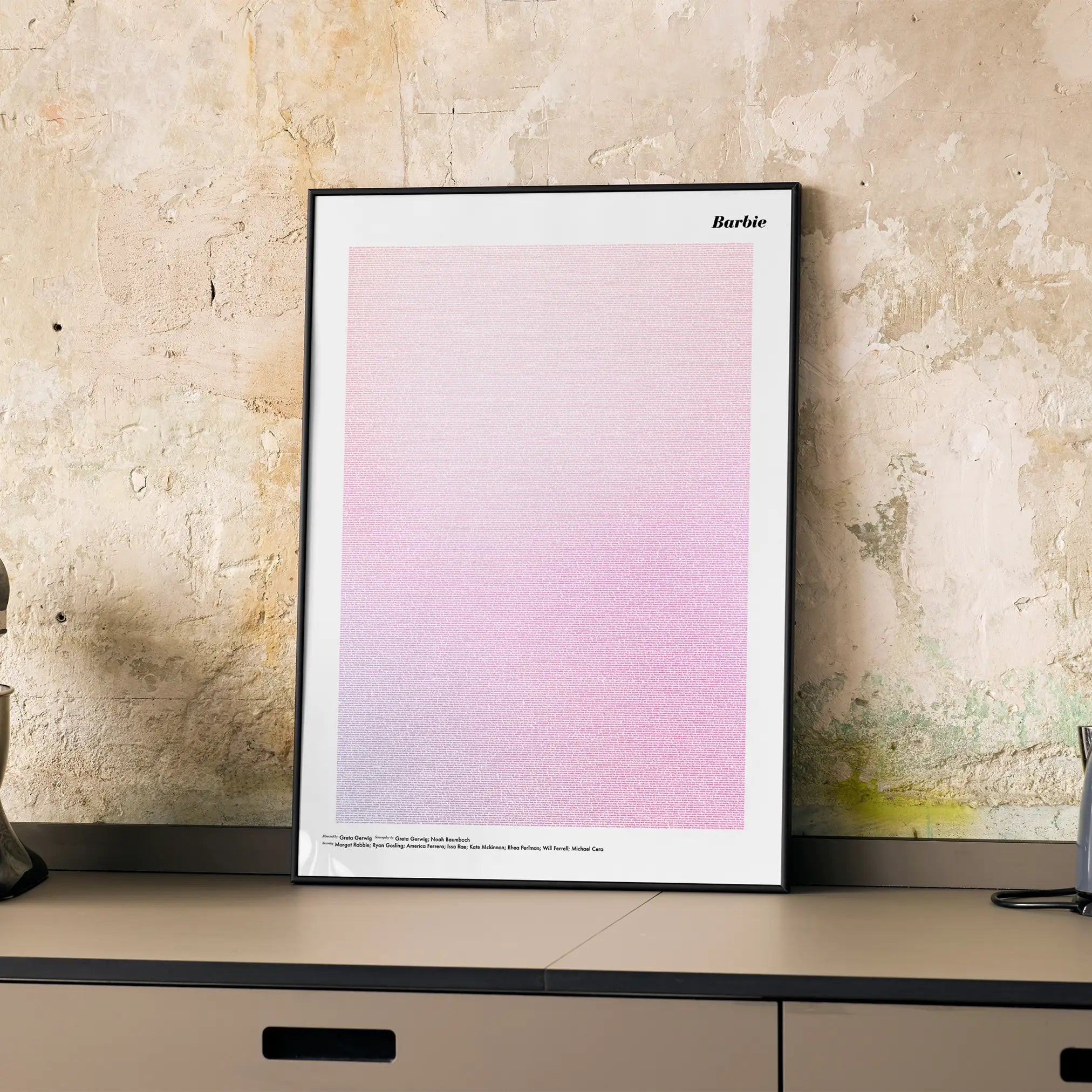 A framed Barbie movie script poster displayed on a cabinet in a minimalist interior.