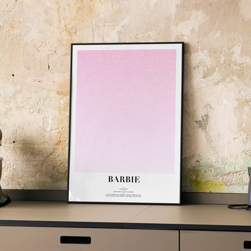 A framed Barbie movie script poster displayed on a cabinet in a minimalist interior.