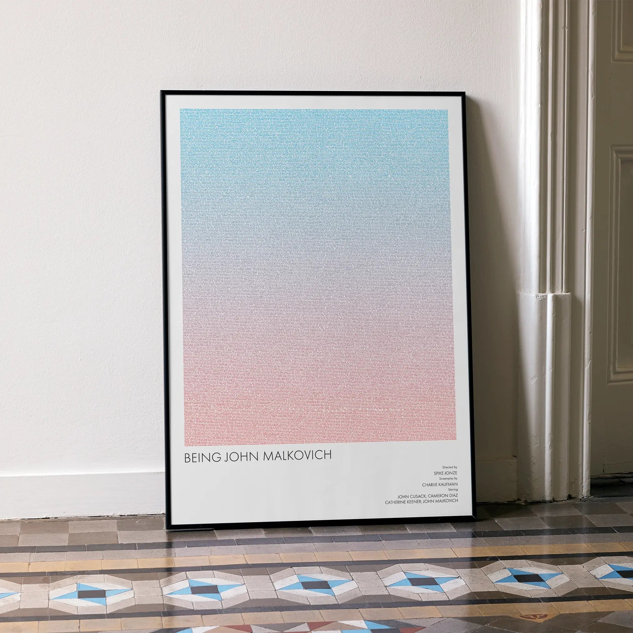 A framed Being John Malkovich movie script poster leaning against a wall in a minimalist interior.