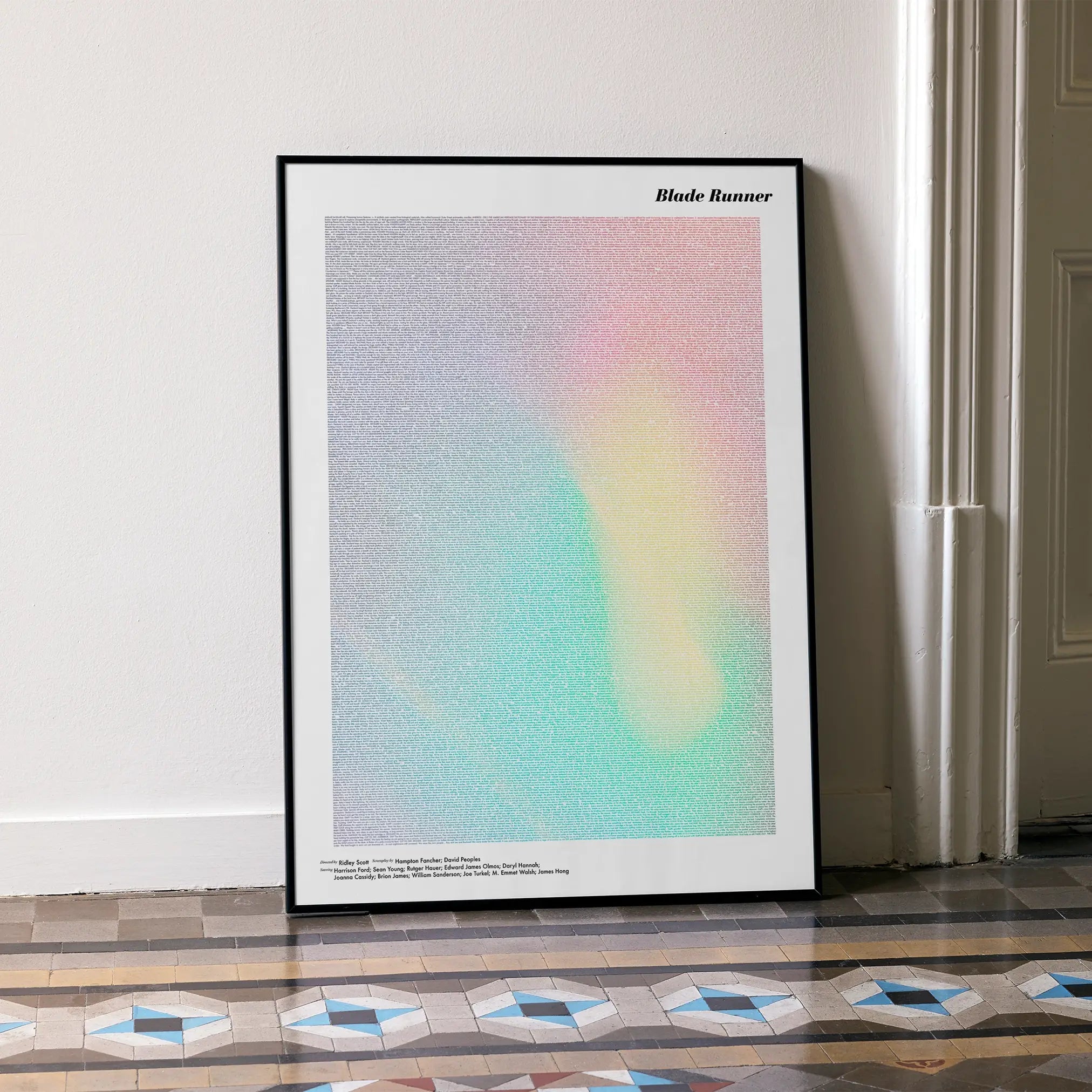 A framed Blade Runner movie script poster leaning against a wall in a minimalist interior.