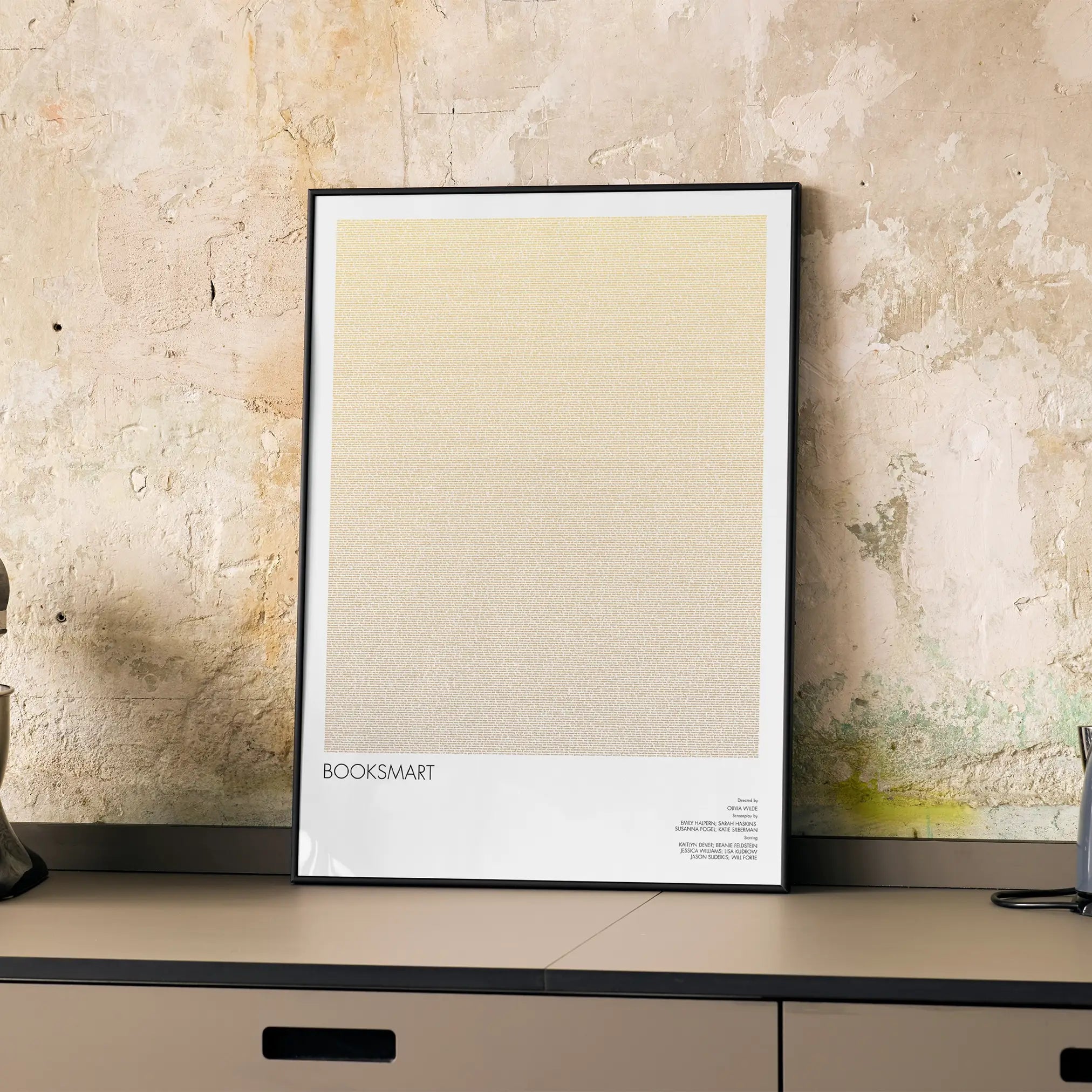 A framed Booksmart movie script poster displayed on a cabinet in a minimalist interior.