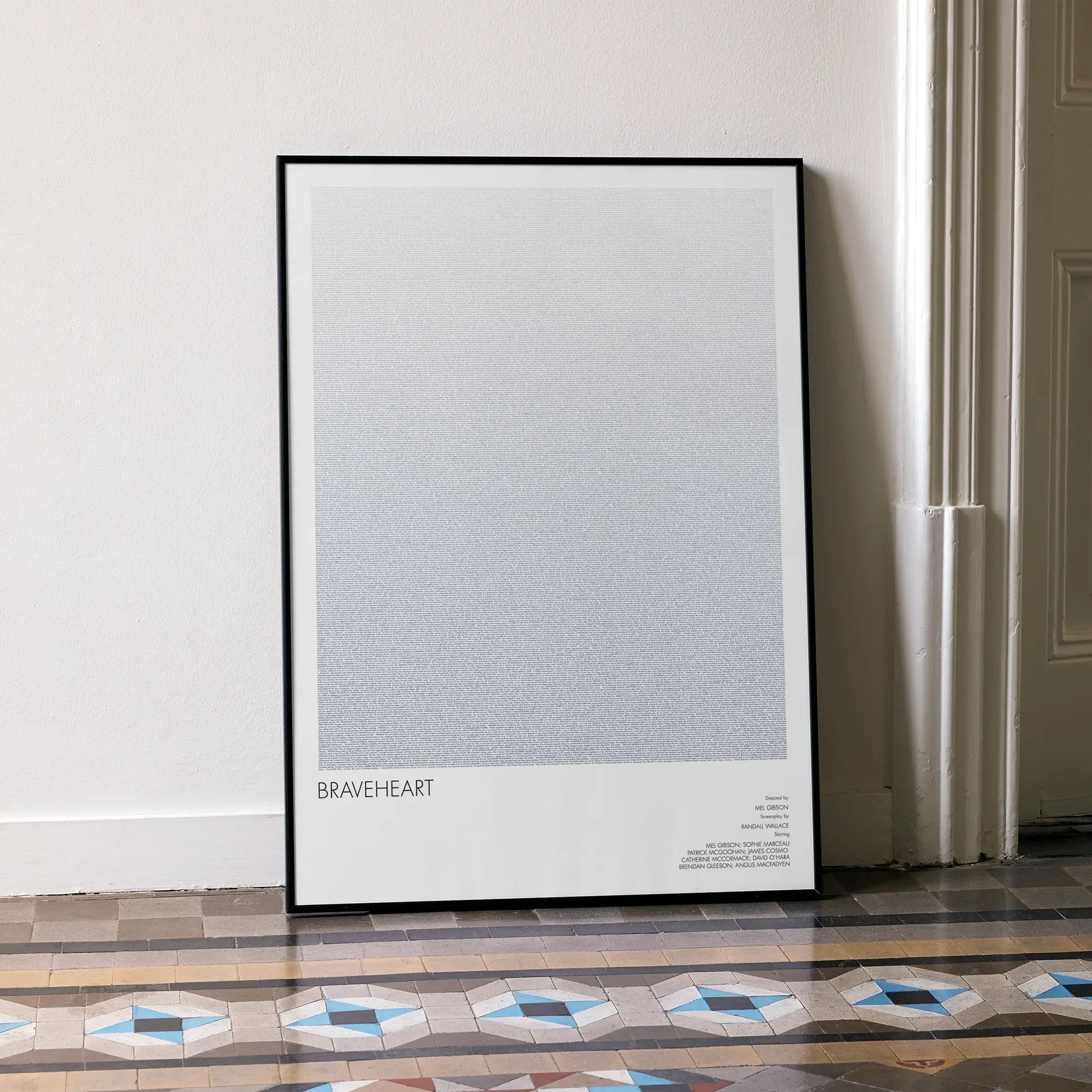 A framed Braveheart movie script poster leaning against a wall in a minimalist interior.