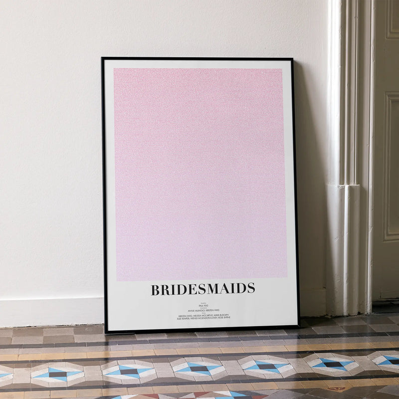 A framed Bridesmaids movie script poster leaning against a wall in a minimalist interior.