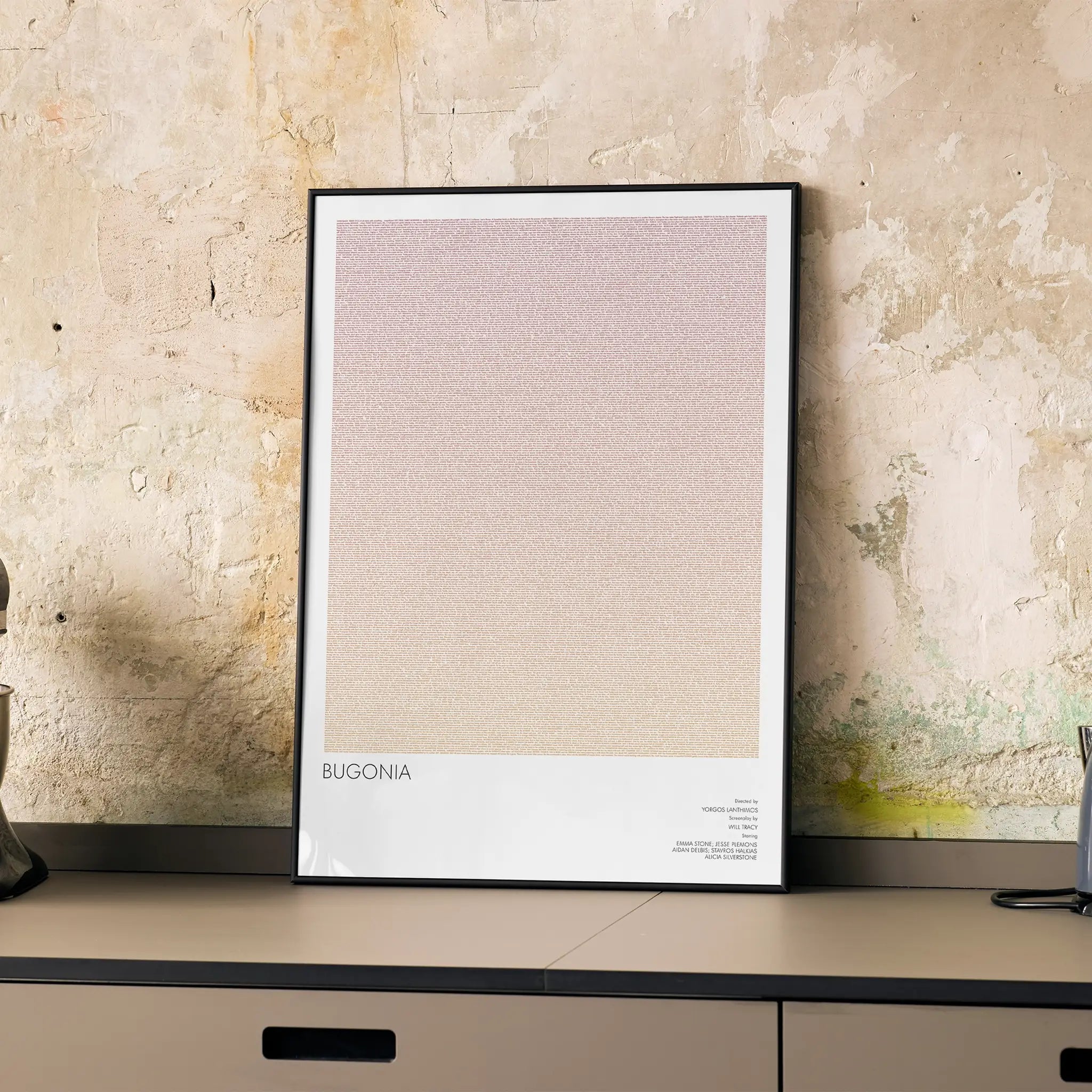 A framed Bugonia movie script poster displayed on a cabinet in a minimalist interior.