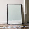 A framed Call Me by Your Name movie script poster leaning against a wall in a minimalist interior.