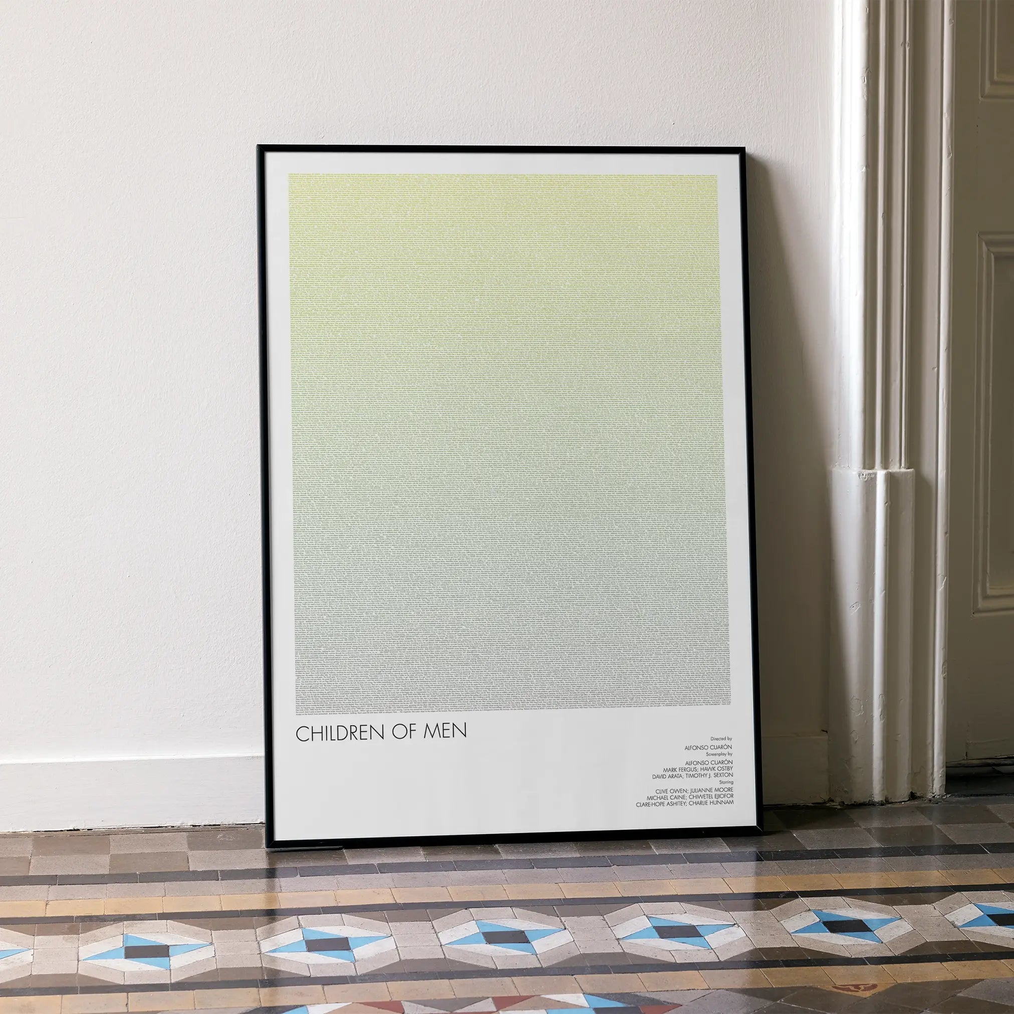 A framed Children of Men movie script poster leaning against a wall in a minimalist interior.