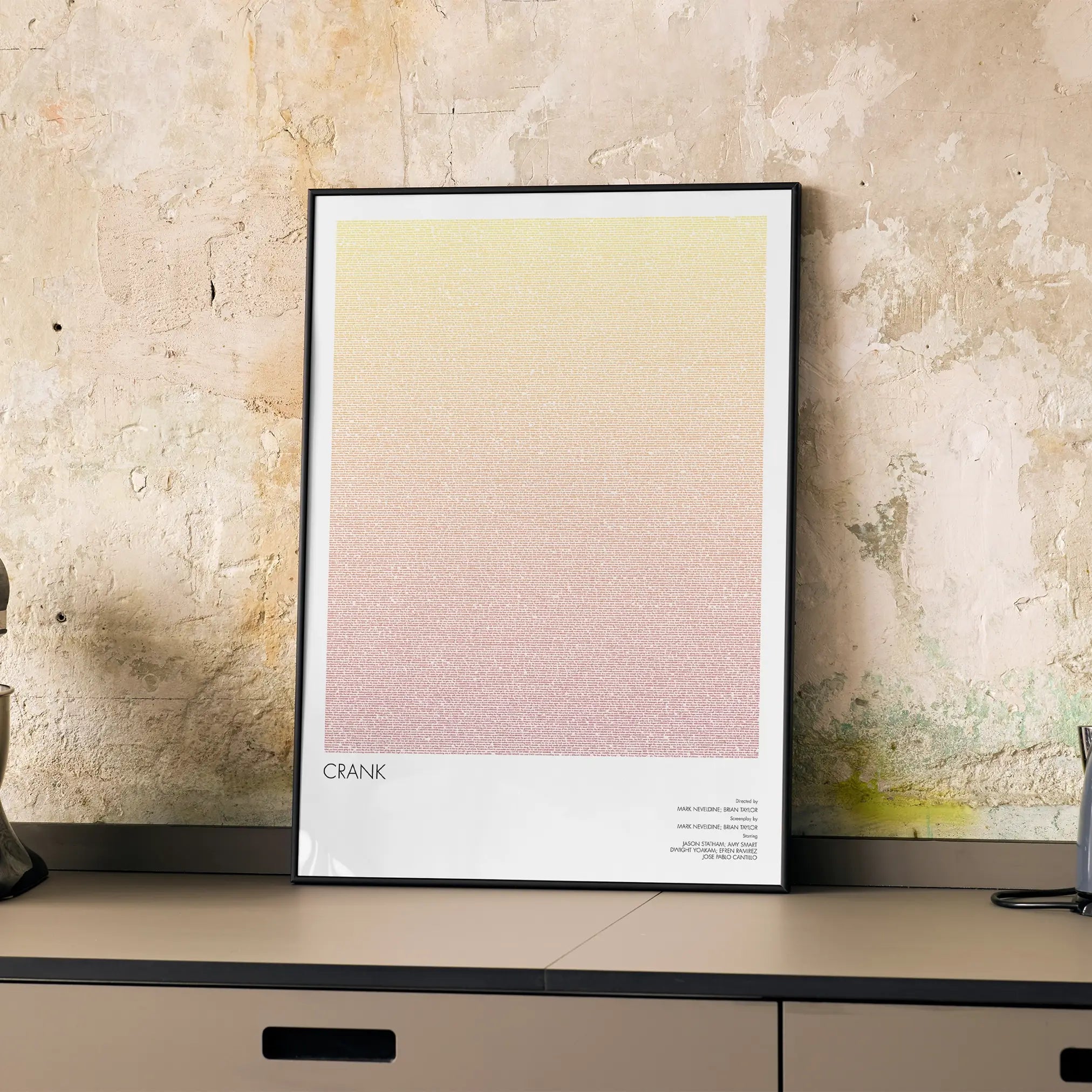 A framed Crank movie script poster displayed on a cabinet in a minimalist interior.