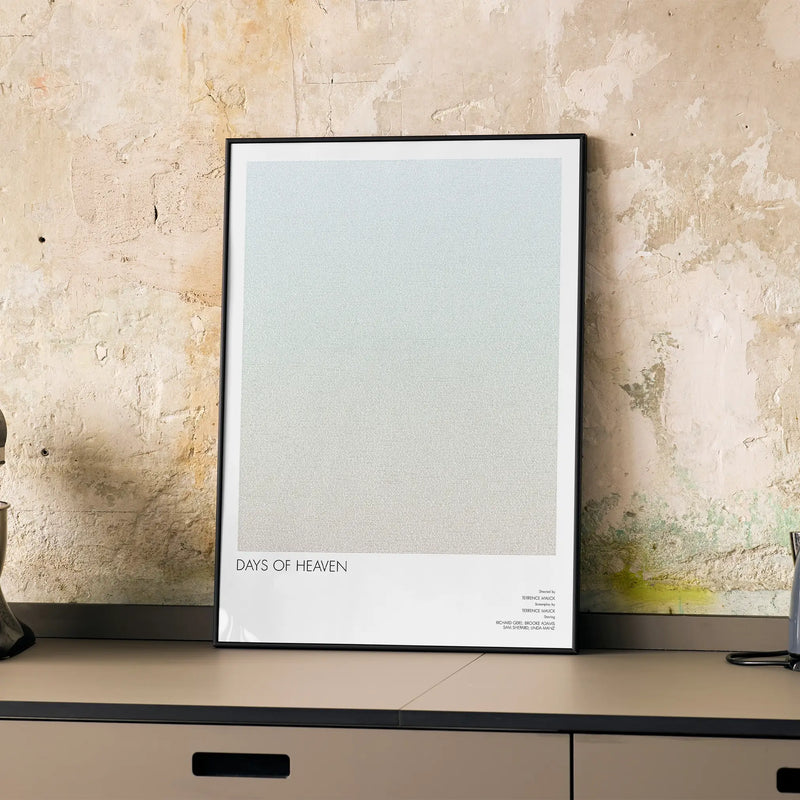 A framed Days of Heaven movie script poster displayed on a cabinet in a minimalist interior.