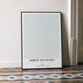A framed Dirty Dancing movie script poster leaning against a wall in a minimalist interior.