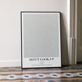 A framed Don't Look Up movie script poster leaning against a wall in a minimalist interior.
