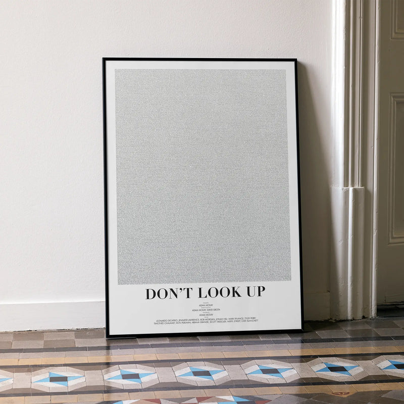 A framed Don't Look Up movie script poster leaning against a wall in a minimalist interior.