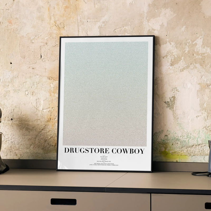 A framed Drugstore Cowboy movie script poster displayed on a cabinet in a minimalist interior.