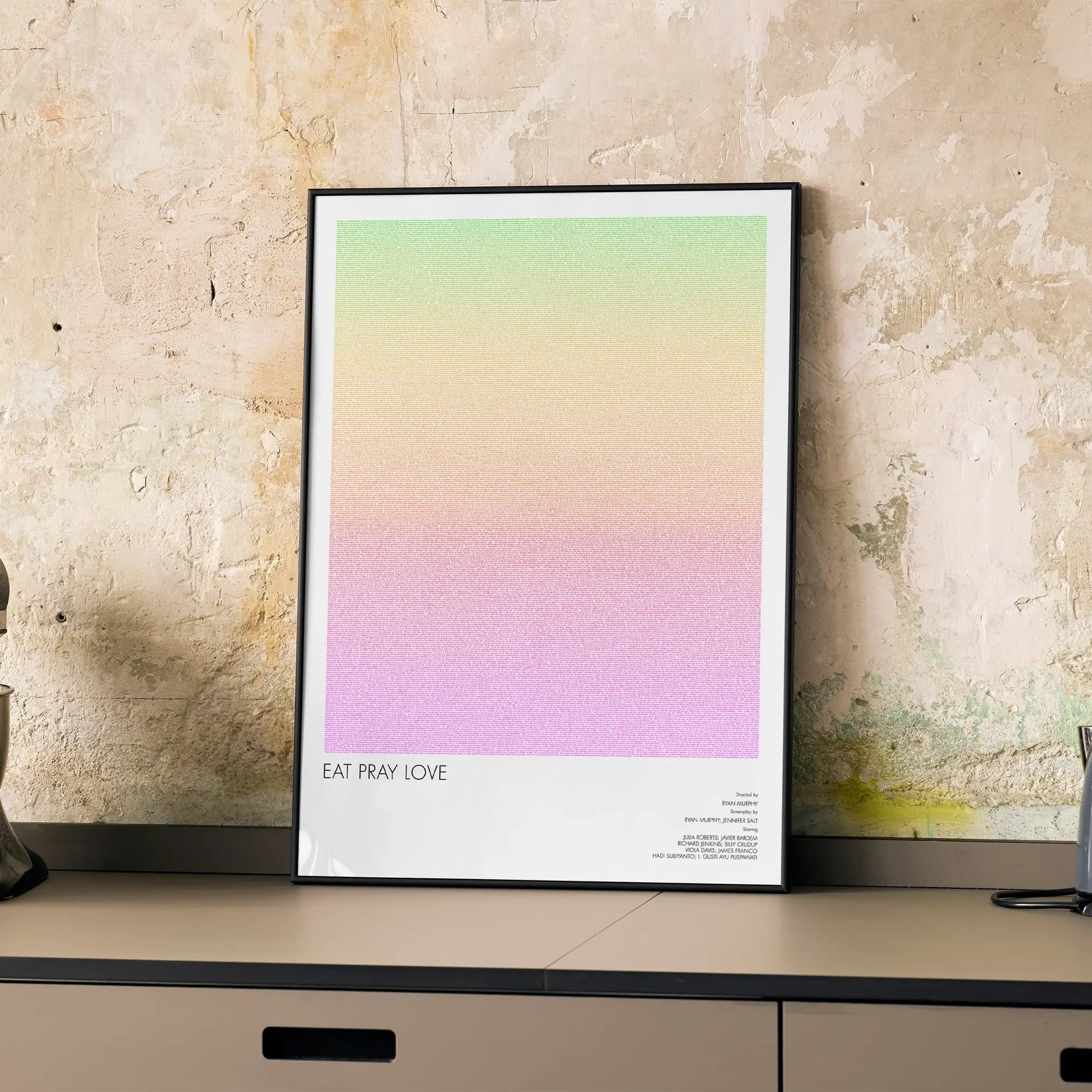 A framed Eat Pray Love movie script poster displayed on a cabinet in a minimalist interior.