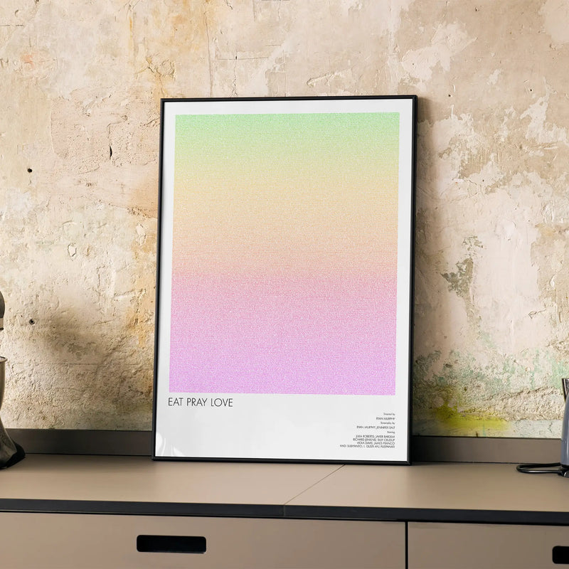 A framed Eat Pray Love movie script poster displayed on a cabinet in a minimalist interior.