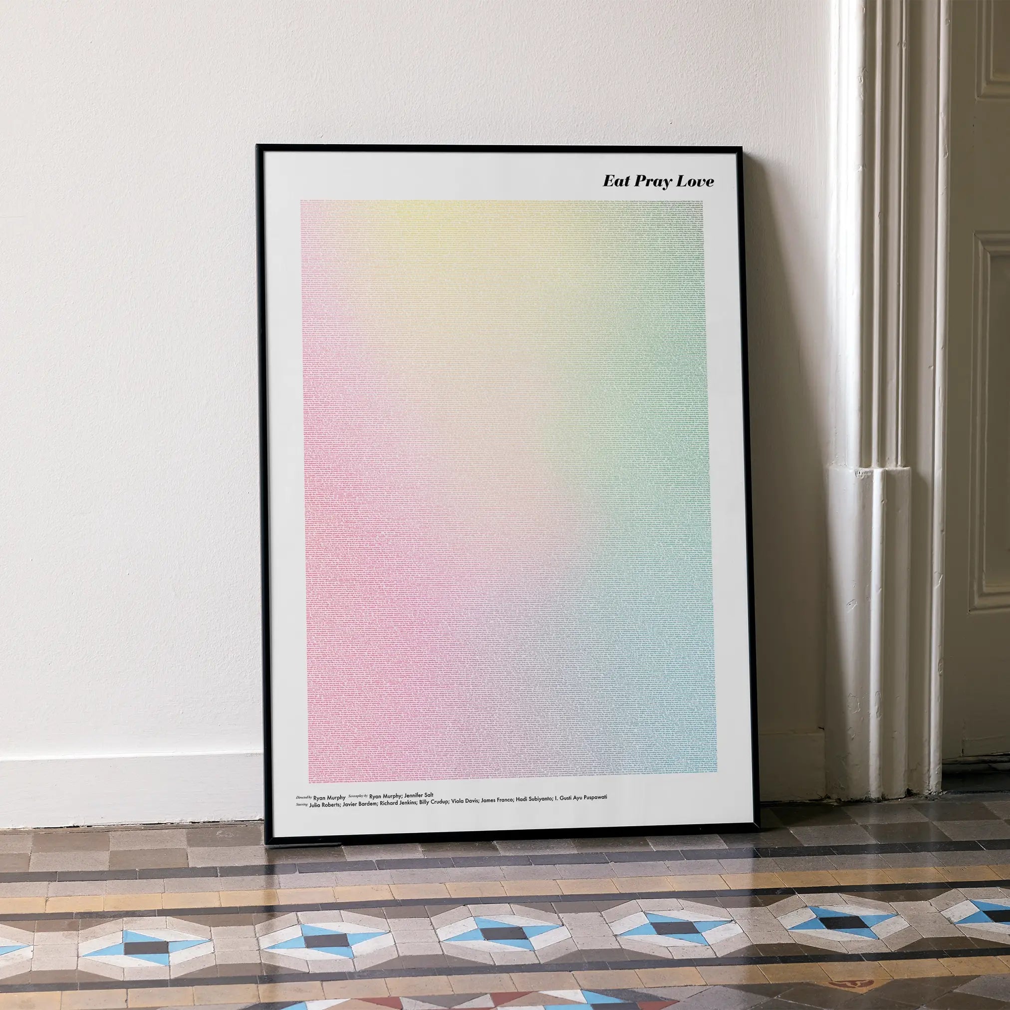 A framed Eat Pray Love movie script poster leaning against a wall in a minimalist interior.