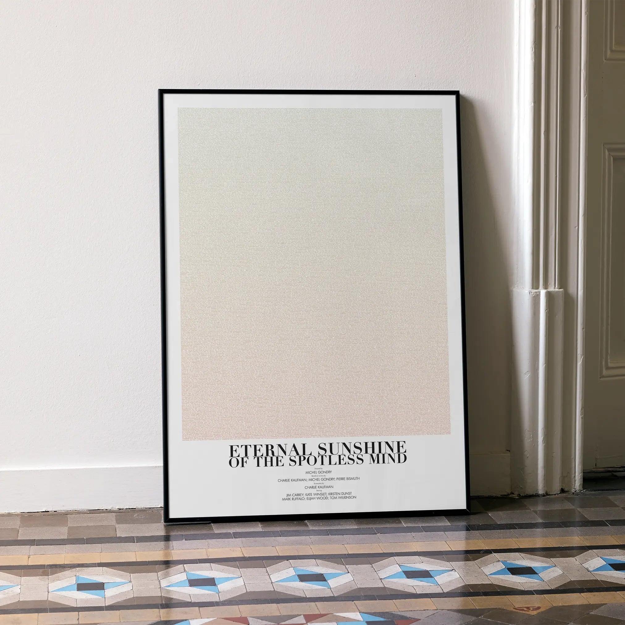 A framed Eternal Sunshine of the Spotless Mind movie script poster leaning against a wall in a minimalist interior.