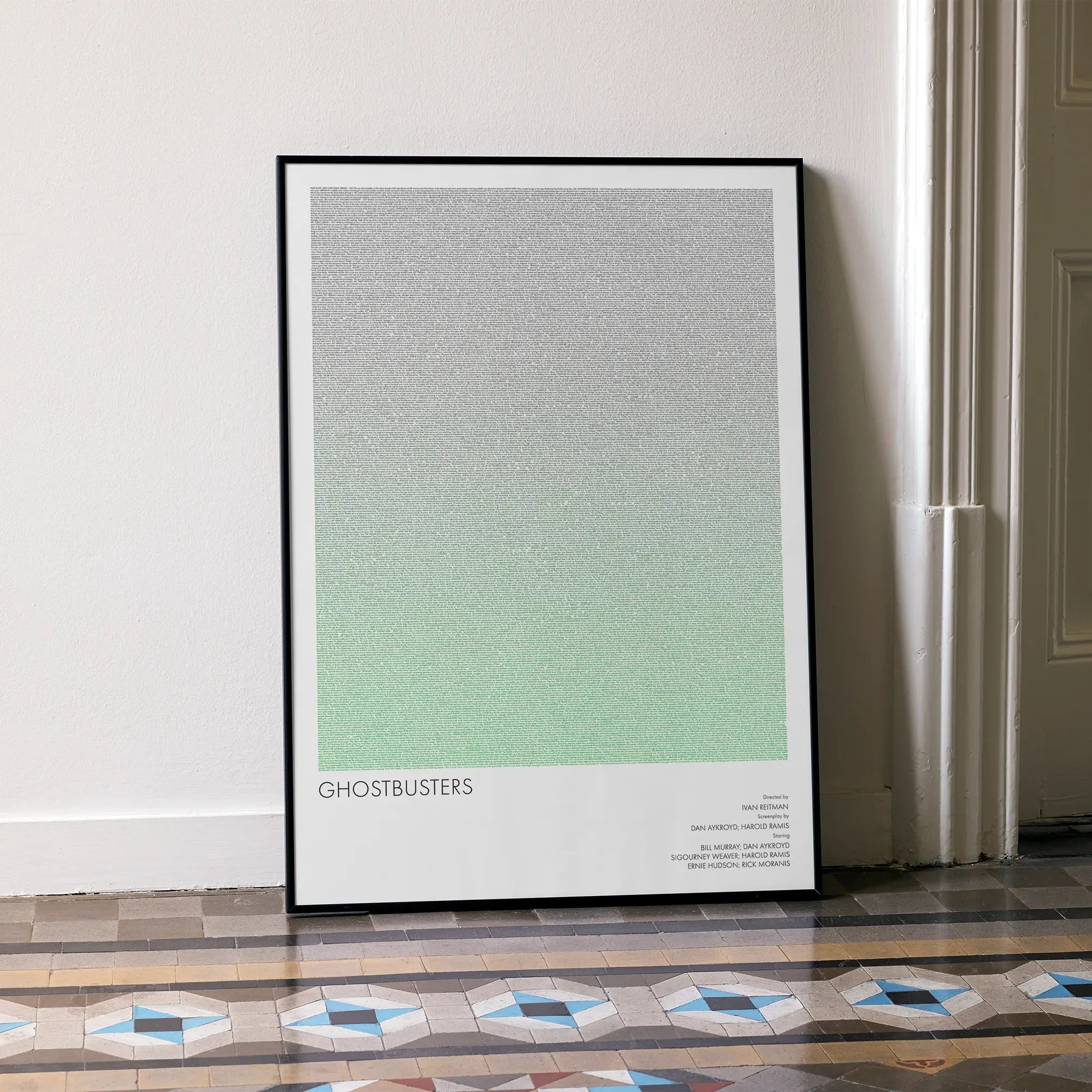 A framed Ghostbusters movie script poster leaning against a wall in a minimalist interior.