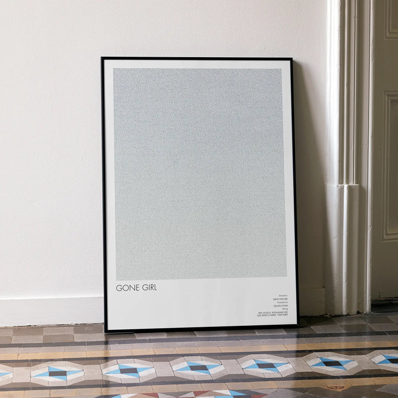A framed Gone Girl movie script poster leaning against a wall in a minimalist interior.