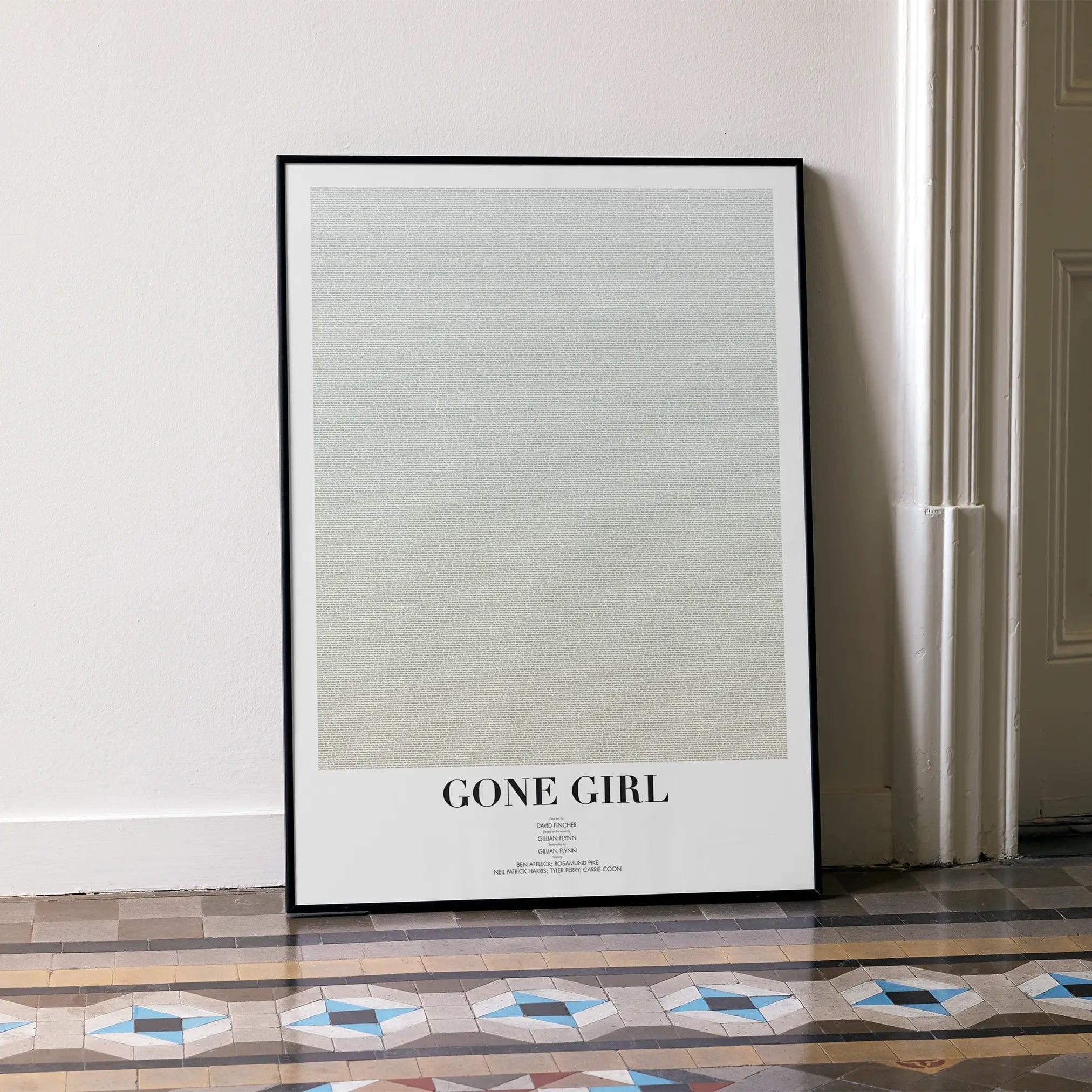 A framed Gone Girl movie script poster leaning against a wall in a minimalist interior.