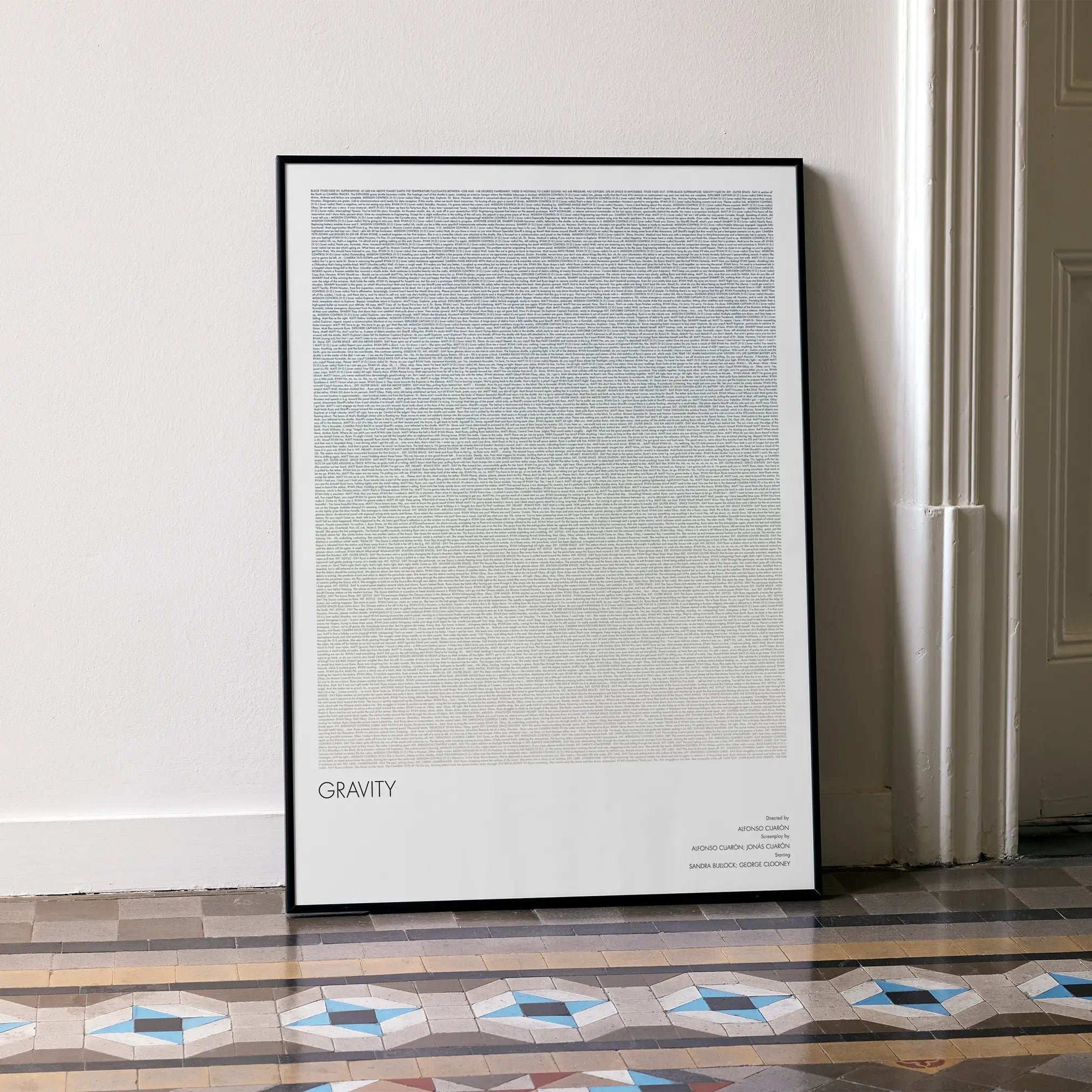 A framed Gravity movie script poster leaning against a wall in a minimalist interior.