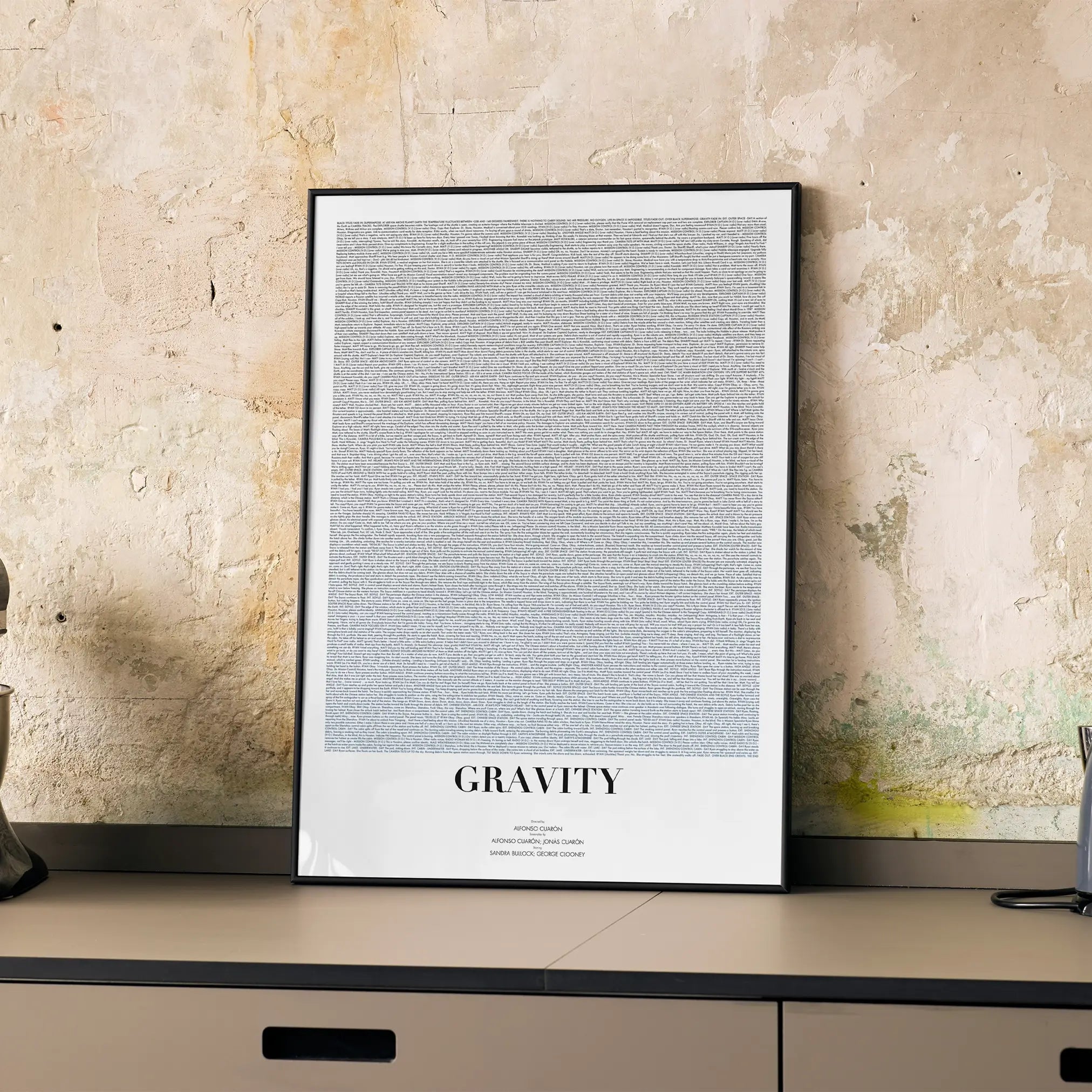 A framed Gravity movie script poster displayed on a cabinet in a minimalist interior.