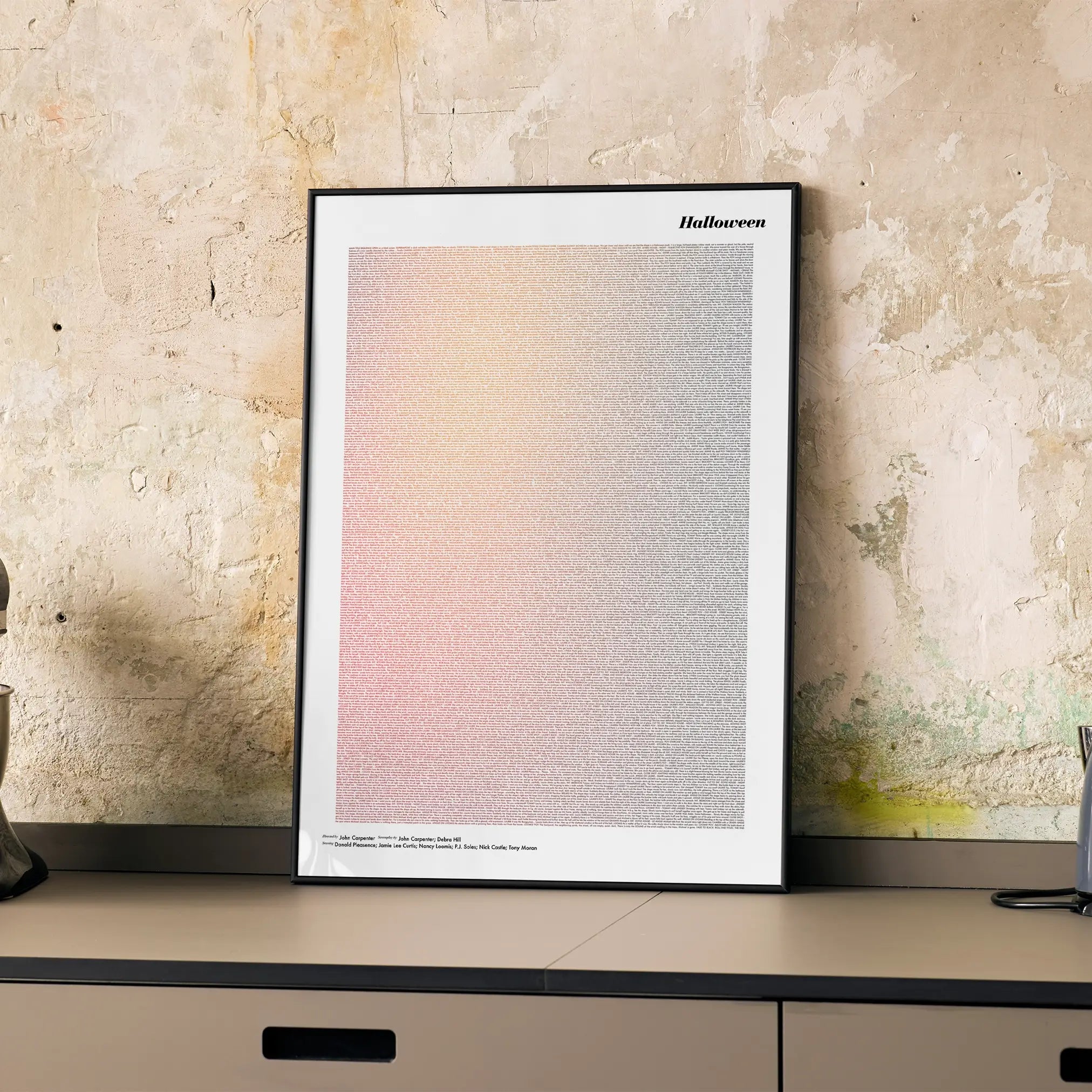 A framed Halloween movie script poster displayed on a cabinet in a minimalist interior.