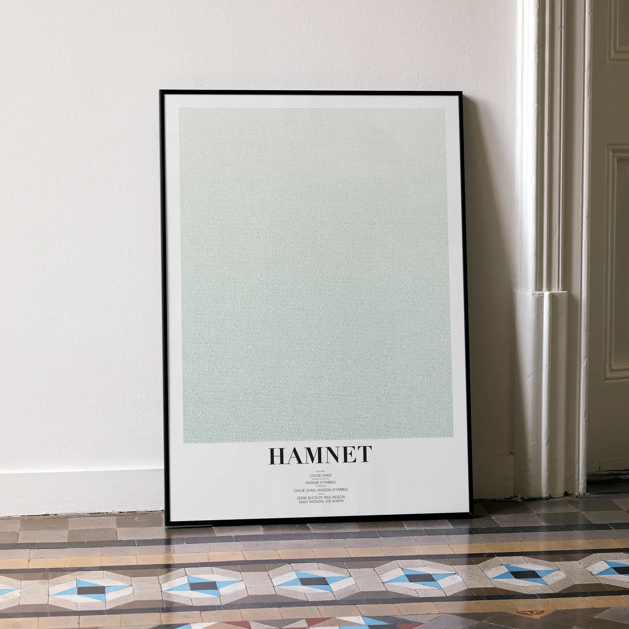 A framed Hamnet movie script poster leaning against a wall in a minimalist interior.