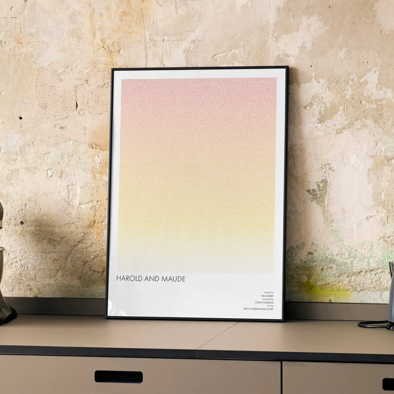 A framed Harold and Maude movie script poster displayed on a cabinet in a minimalist interior.